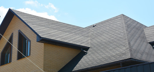 A close-up on a roof problem area covered with asphalt roof shingles and irregular shape window on the wall of the house construction. - obrazy, fototapety, plakaty