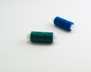 Fototapeta na wymiar two reels of green and blue sewing thread on a white background