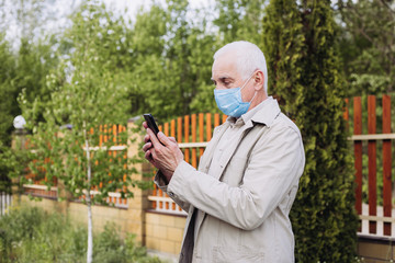 senior man with medical face mask using the phone to search for news