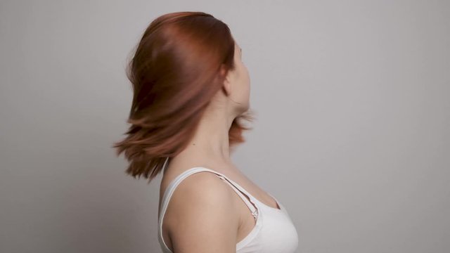 Girl taking off rubber band from red hair after a long daily routine. Grey background
