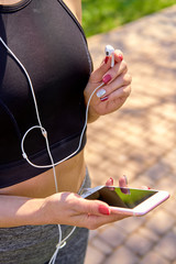 Runner girl holding smartphone using touchscreen for choosing music or texting sms on app before running on track. Closeup hand of woman using smartphone with headphones. Smartphone apps concept. Fema