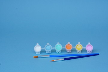 Cans of colored acrylic or watercolor paint and brushes on blue background, set for creativity with...