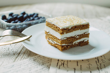 Honey cake with blueberries in a white saucer on the table