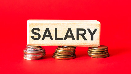 Salary text written on a wooden block with folded coins on a red background