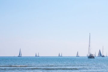 Many sail yachts in the sea in the backdrop bright sunshine. Calm weather. Romantic magical summer.
