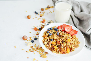 Healthy breakfast - organic granola with honey, oatmeal, cashew nut, almond, raisin and strawberries, blueberries in white plate with glass of milk and spoon. The concept of diet. copy space