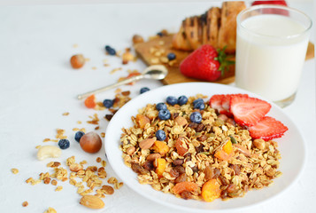 Healthy breakfast - organic granola with honey, oatmeal, cashew nut, almond, raisin and strawberries, blueberries in white plate with glass of milk and spoon. The concept of diet. copy space