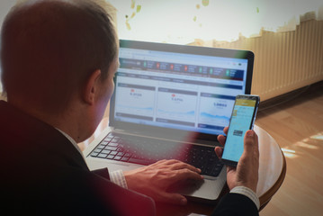 Businessman analysing stock market exchanges from phone and laptop at home