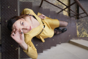 Young woman sitting on city stairs wearing a yellow dress posing. City street fashion