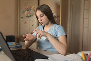 Teenager girl 12-15 years old, antiseptic spray protection against viruses, home bottle in hand, laptop lessons. E-education and distance learning through Internet and video communications.