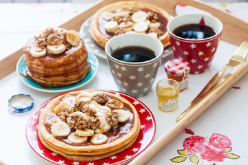 Breakfast tray with pancakes with bananas, maple syrup and nuts, cup of coffee and honey.