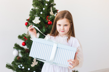 Child girl opens gift box near Christmas tree. Holidays, christmas time and presents concept.