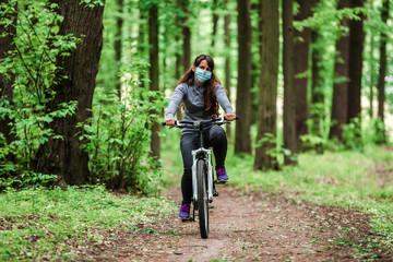 woman in medical mask rides a bicycle in the park