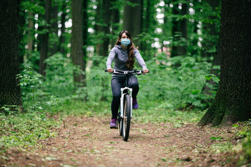 Fototapeta na wymiar woman in medical mask rides a bicycle in the park