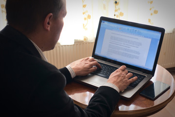 Senior academician working from home writing essay from his laptop on a table