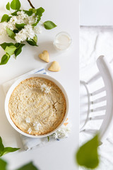 Plate with whole cheesecake pie on table with lilacs. Classic cheesecake flat lay, top view.