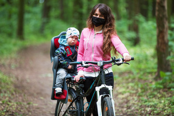 Fototapeta na wymiar girl with a child riding a bicycle in a medical mask on her face
