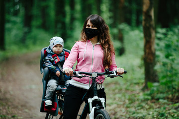 Fototapeta na wymiar girl with a child riding a bicycle in a medical mask on her face