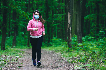 woman in a medical mask runs in the forest. Stay in fit during quarantine. Coronavirus pandemic Covid-19