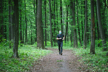 Obraz premium Runner wearing medical mask. Coronavirus pandemic Covid-19 a man in a medical mask runs in the forest