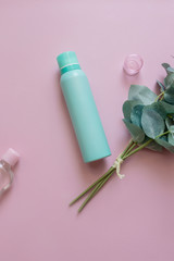 Close-up view of an aquamarine aluminum jar of perfume spray deodorant with a green plant. Green metal bottle flat lay on a pink background. An aerosol can image. A cosmetic bottle for beauty needs.