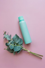 Close-up view of an aquamarine aluminum jar of perfume spray deodorant with a green plant. Green metal bottle flat lay on a pink background. A cosmetic bottle for beauty needs. An aerosol can image.