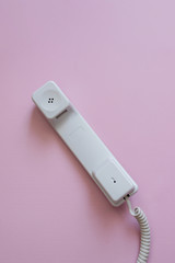 A close up view of A white vintage dial telephone handset on pink background. Communication device. A retro receiver with phone curly wire and copy space. Office context. Call center.