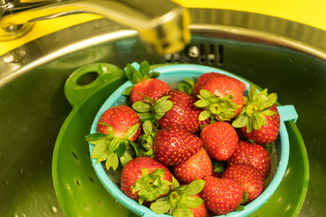 Strawberry bowl in a colander washing on the tap with wáter / Bol de fresas en un colador lavándose en el grifo con agua 