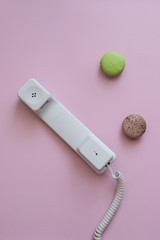 A close up view of A white vintage dial telephone handset and two macaronis on pink background. Communication device. A retro receiver with phone curly wire and copy space. Office context. Call center