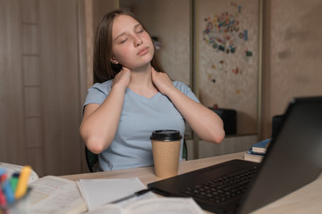 Fototapeta na wymiar Tired kneading neck, muscle pain, teenager girl 12-15 years old, rest after hard lesson, home laptop. E-education and distance learning Internet and video communications. A cup of coffee with tea.