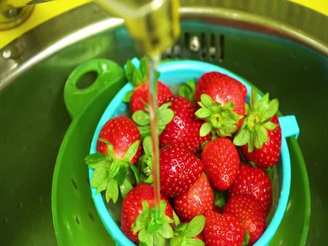 Strawberry bowl in a colander washing on the tap with w&aacute;ter / Bol de fresas en un colador lav&aacute;ndose en el grifo con agua