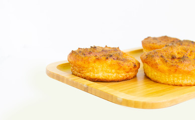 Wooden board with delicious rosy cupcakes on a white plate, top view.
