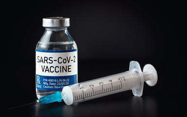 Coronavirus Covid 19 vaccine concept (own design, not real product) - small glass bottle with silver cap, syringe near, closeup detail on black background