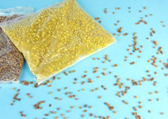 Plastic portion bags with buckwheat and barley. Scattered buckwheat on blue background.                                                             
