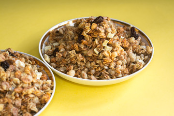 muesli fried cereals in a plate gold dried fruits raisins on a yellow background place for text