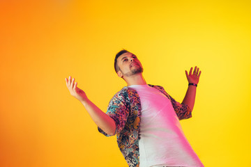 Young caucasian musician in casual dancing on gradient yellow background in neon light. Concept of music, hobby, festival. Joyful party host, DJ, stand upper, dancer. Colorful portrait of artist.