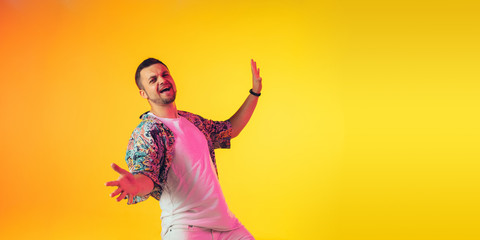 Fototapeta na wymiar Young caucasian musician in casual dancing on gradient yellow background in neon light. Concept of music, hobby, festival. Joyful party host, DJ, stand upper, dancer. Colorful portrait of artist.