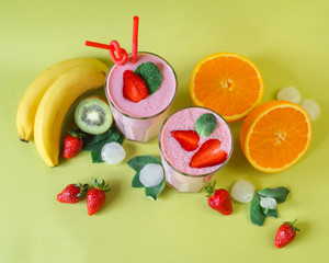 two glasses of cocktail with mint and strawberries on top. around different fruits and ice (banana, orange, kiwi, strawberries)