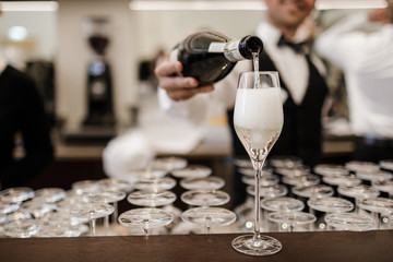 The waiter pours champagne into the glass. A beautiful picture of champagne in a glass. A glass of champagne in the foreground. 
