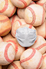 Covid-19 and Sports Concept. Closeup of a pile of old used baseballs in vertical format with one ball wearing a surgical mask.