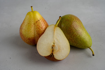 Two whole ripe pears and one half of a pear are laying on concrete surface