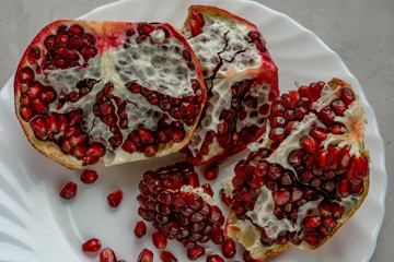 Pomegranate slices and pomegranate seeds are laying on white plate