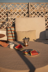 authentic spring-summer morning breakfast or brunch at the terrace with fresh watermelon fruit slices, coffee, and a hand holding a vintage coffee mug, hit by beautiful sunlight © mafergonzalezphoto