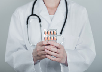 Medical doctor holding strip of pills on grey hospital wall background.