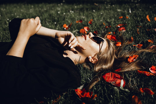 a beautiful young girl in a black dress lies on the green grass, her hair is spread out over the grass; flowers in hair