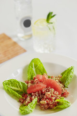 lettuce, quinoa, grapefruit fillet and bell pepper in a white plate, next to water with lemon