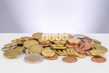 Ein Haufen Euromünzen dauf denen vier Würfel liegen, die das Wort Geld ergeben