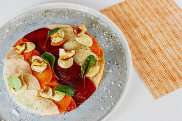 carpaccio of vegetables sprinkled with mushrooms on a white plate next to the menu