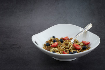 Pancake cereal. Trendy food, mini cereal pancakes in bowl on the table, grey cement background. Trendy baked mini pancakes with strawberries, blueberries . Copy space. Flat layout. Table top view.
