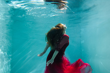Beautiful girl underwater in a red dress swims in the pool. Tenderness and elegance. Bubbles and a...
